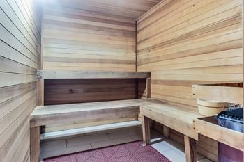 A wooden sauna with benches and a bucket of stones.